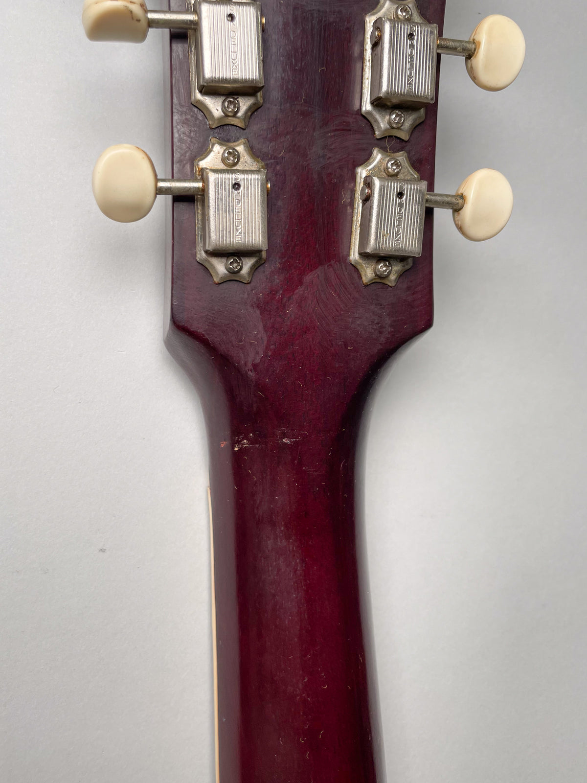 Rear view of the cherry red headstock and neck, showing four cream-buttoned tuners and finish wear on the neck heel.