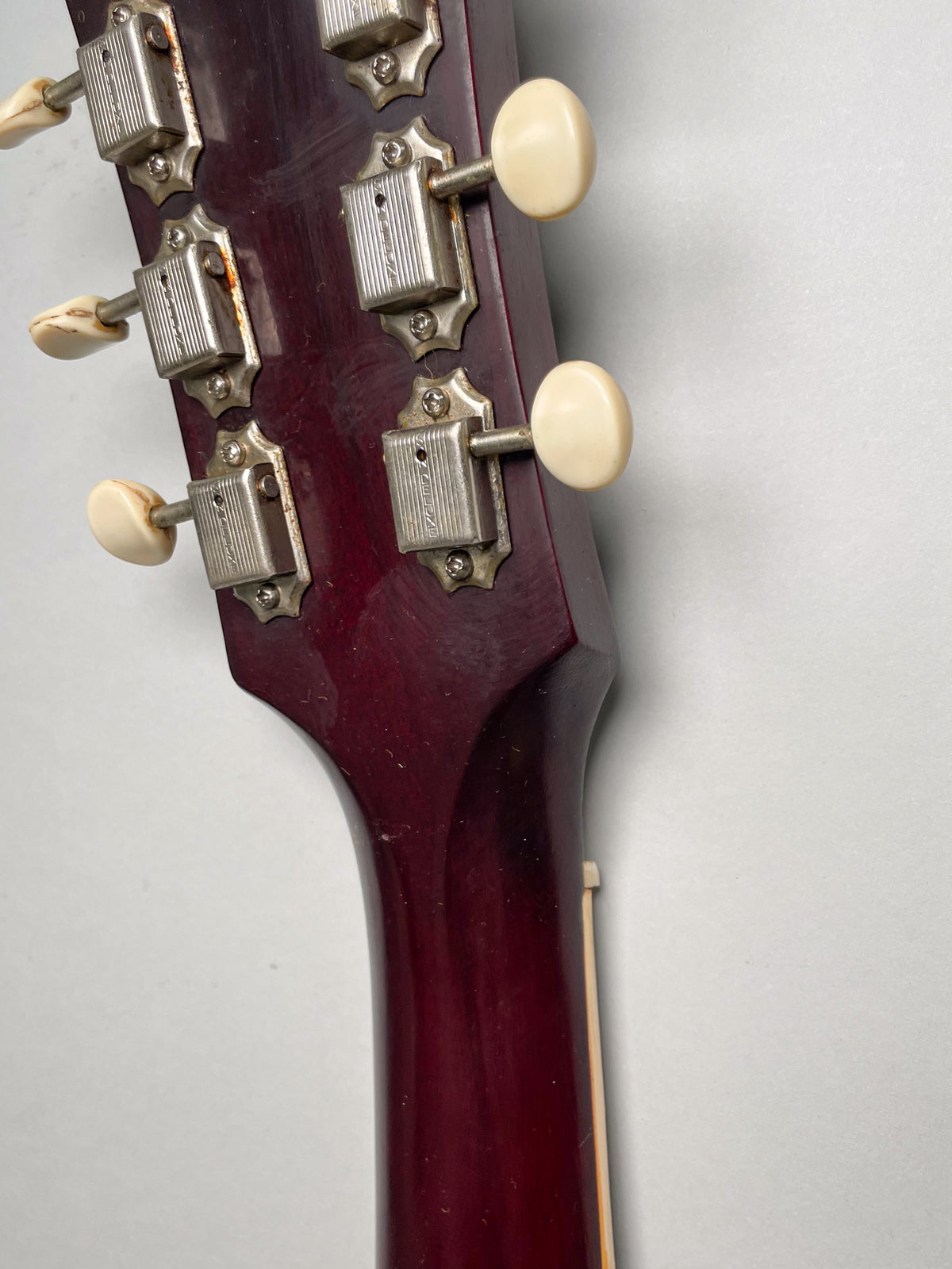 Close-up of the guitar's cherry red headstock and neck, showing six cream tuning pegs with tarnished metal tuners.