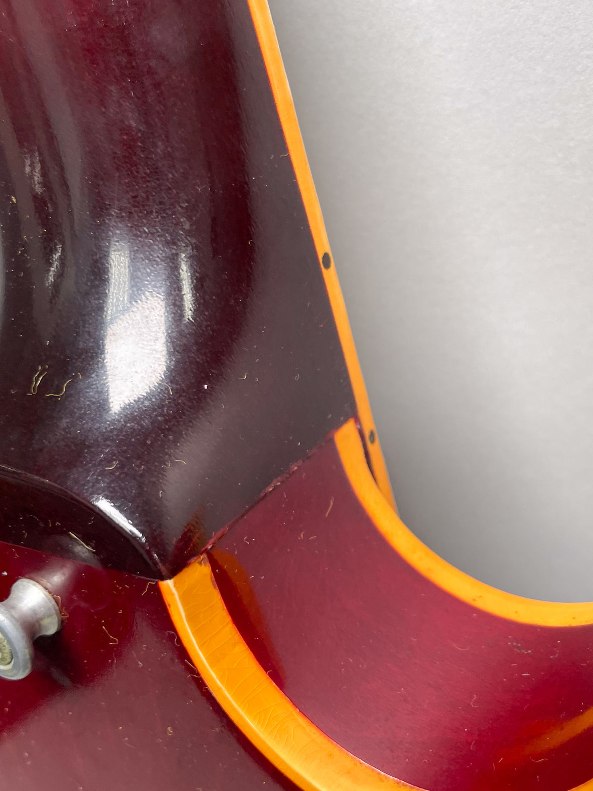 Close-up of the cherry red guitar's neck heel and body joint, showing finish checking, dust, and a strap button.