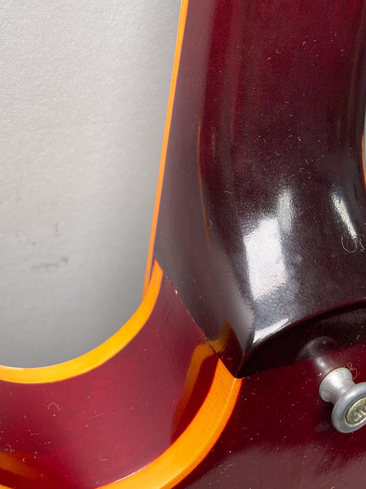 Close-up of the cherry red body's cutaway and neck joint, showing binding, finish checking, and a strap button.