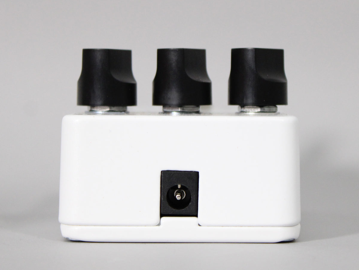 The white reverb pedal is viewed from the back, showing three black control knobs and a centered power input jack.