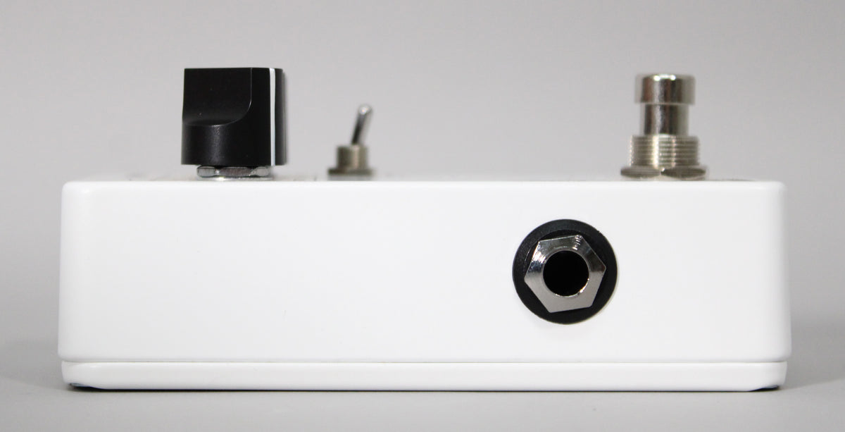The white pedal is viewed from the side, showing a black knob, a small toggle switch, a footswitch, and an input jack.