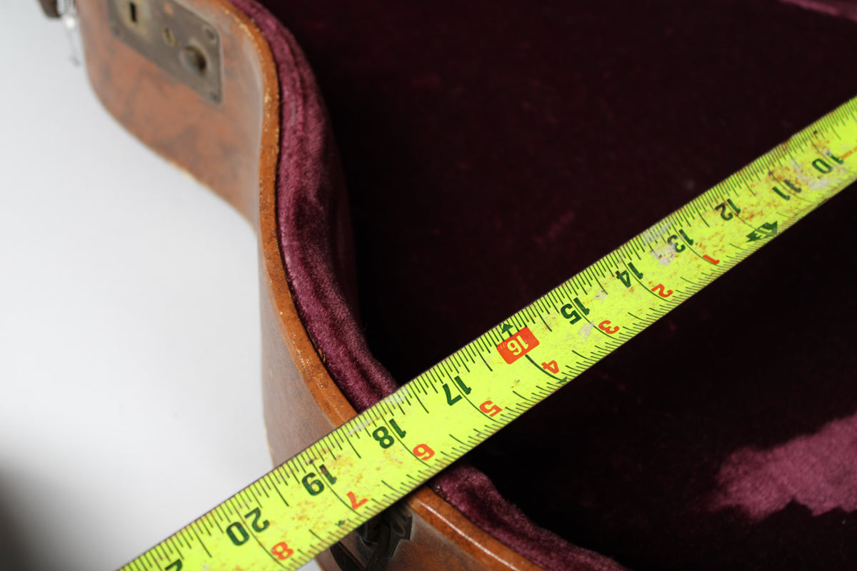 A bright yellow tape measure extends diagonally across the open brown case, showing 10 to 20 inches against the pink velvet interior.