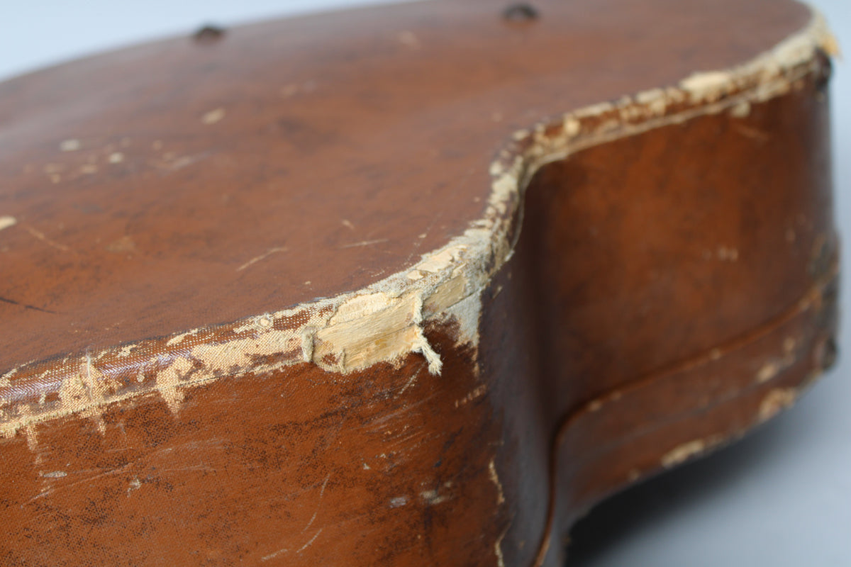 Close-up of the brown archtop case's worn edge, showing significant peeling and fraying of the covering material.