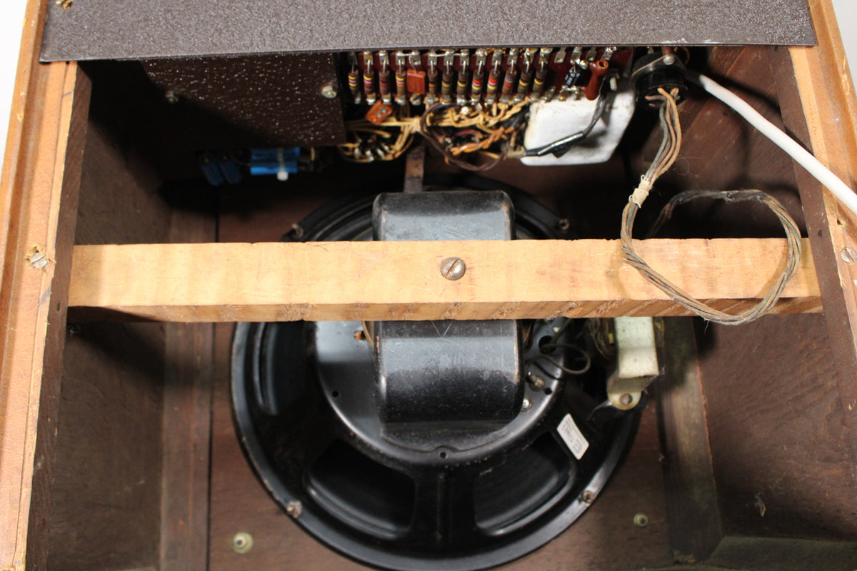 Top-down view of the amp's open back, revealing the black speaker, internal wiring, and a wooden brace across the speaker.
