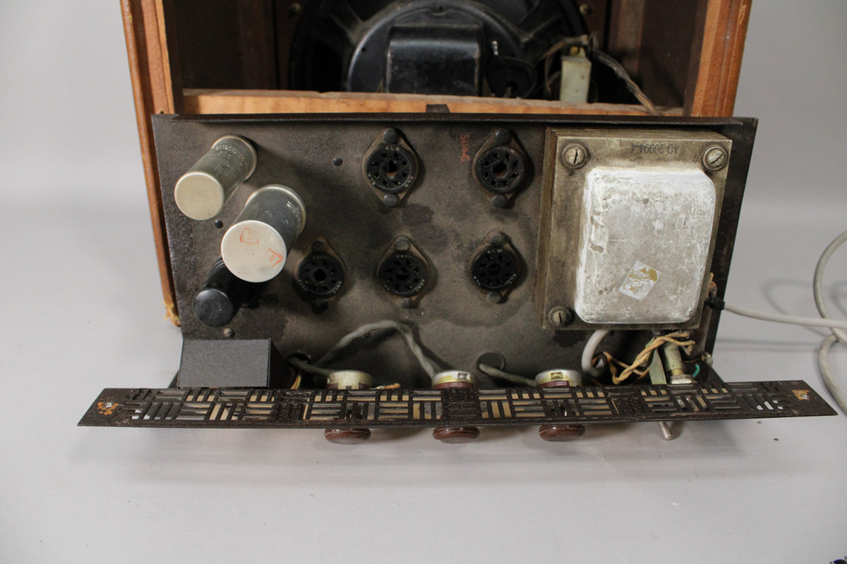 Top-down view of the dusty, dark brown metal chassis, showing four tube sockets, two large capacitors, and a metal transformer.