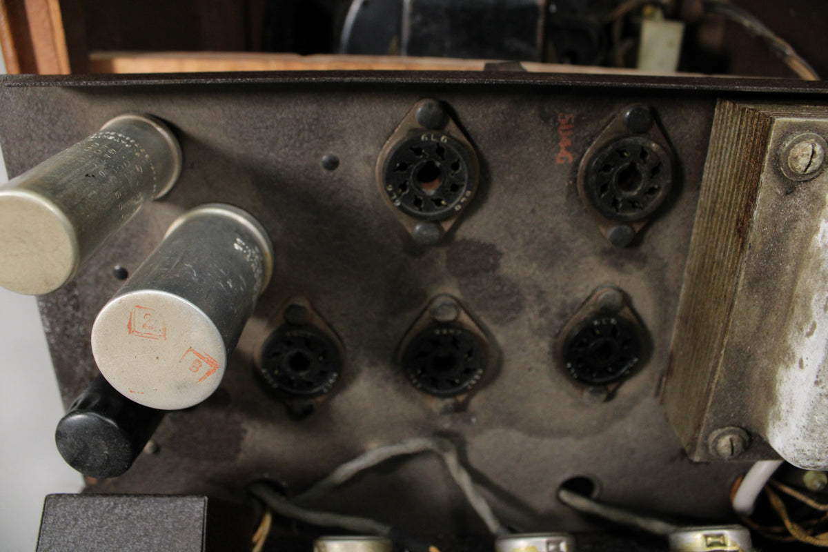 Close-up of the amp's dusty, dark grey chassis, showing six empty tube sockets, two large silver capacitors, and a transformer.