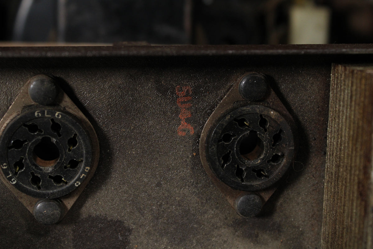 Close-up of two dark, empty tube sockets on a worn, dark metal chassis, with faint red lettering between them.