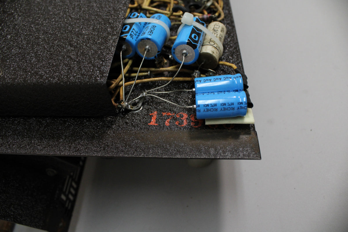 A close-up of the amp's internal wiring, showing several blue capacitors, some secured with white zip ties, and a red "1735" stamp.