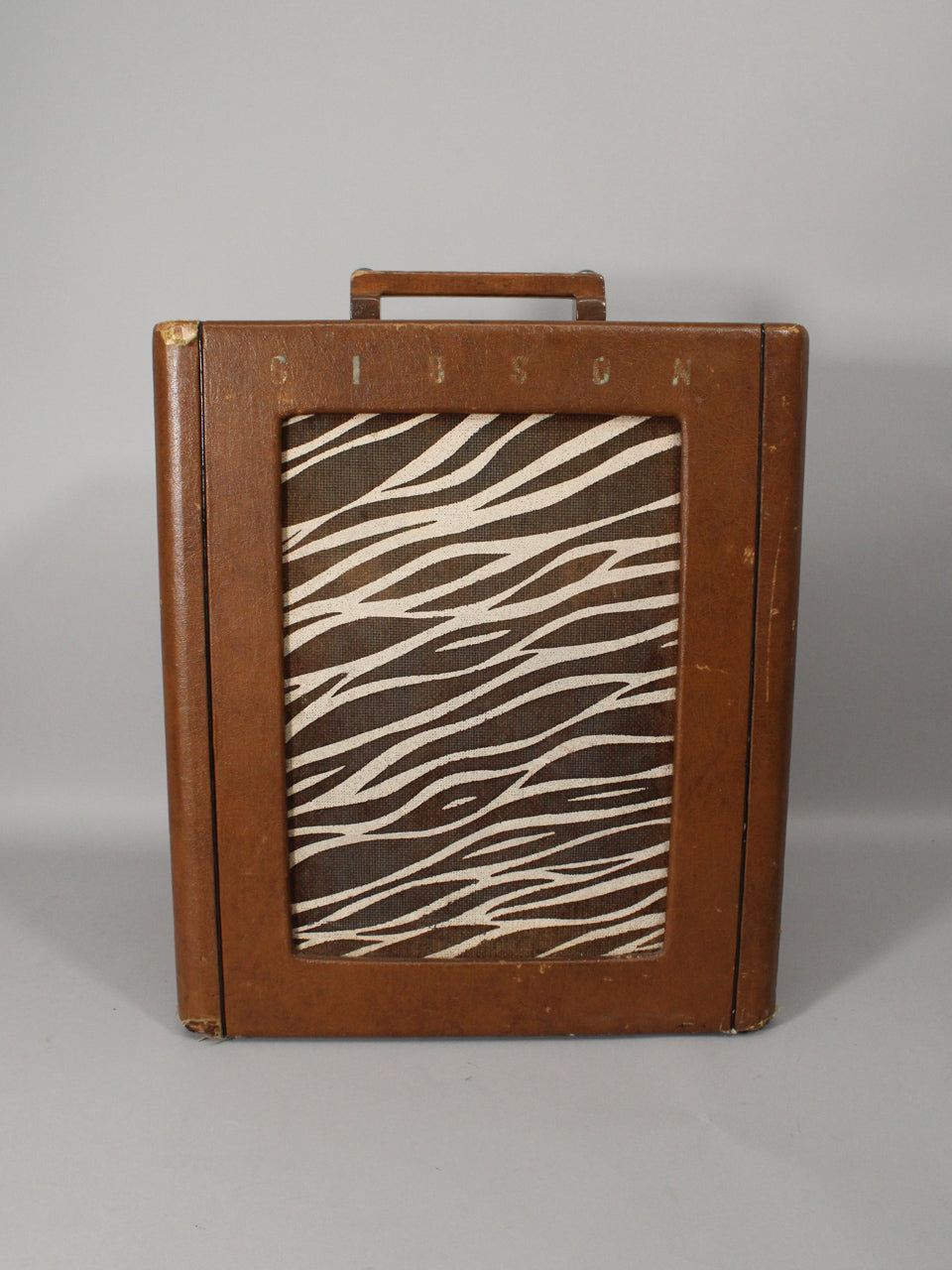 Front view of a vintage brown leatherette combo amp with a zebra-stripe grille cloth and a top handle, showing corner wear.