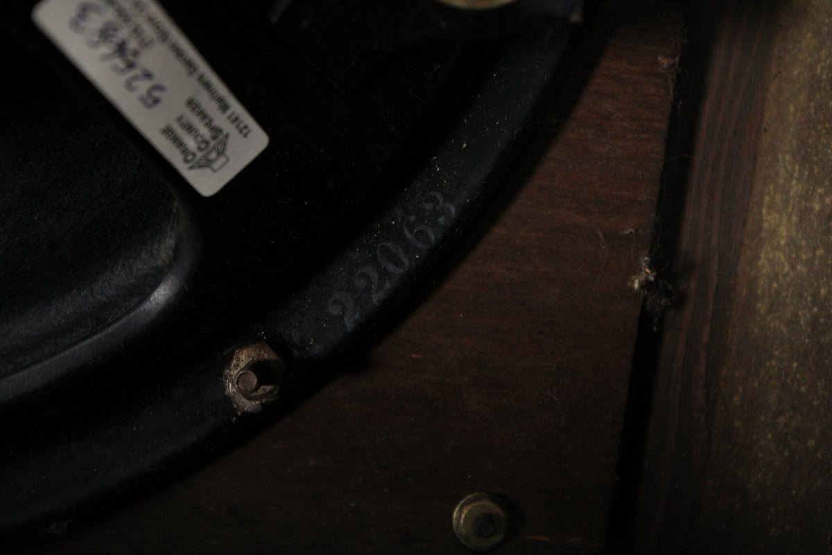 Close-up of the amp's black speaker frame, showing a white label, stamped numbers "22063", and a rusty mounting bolt.