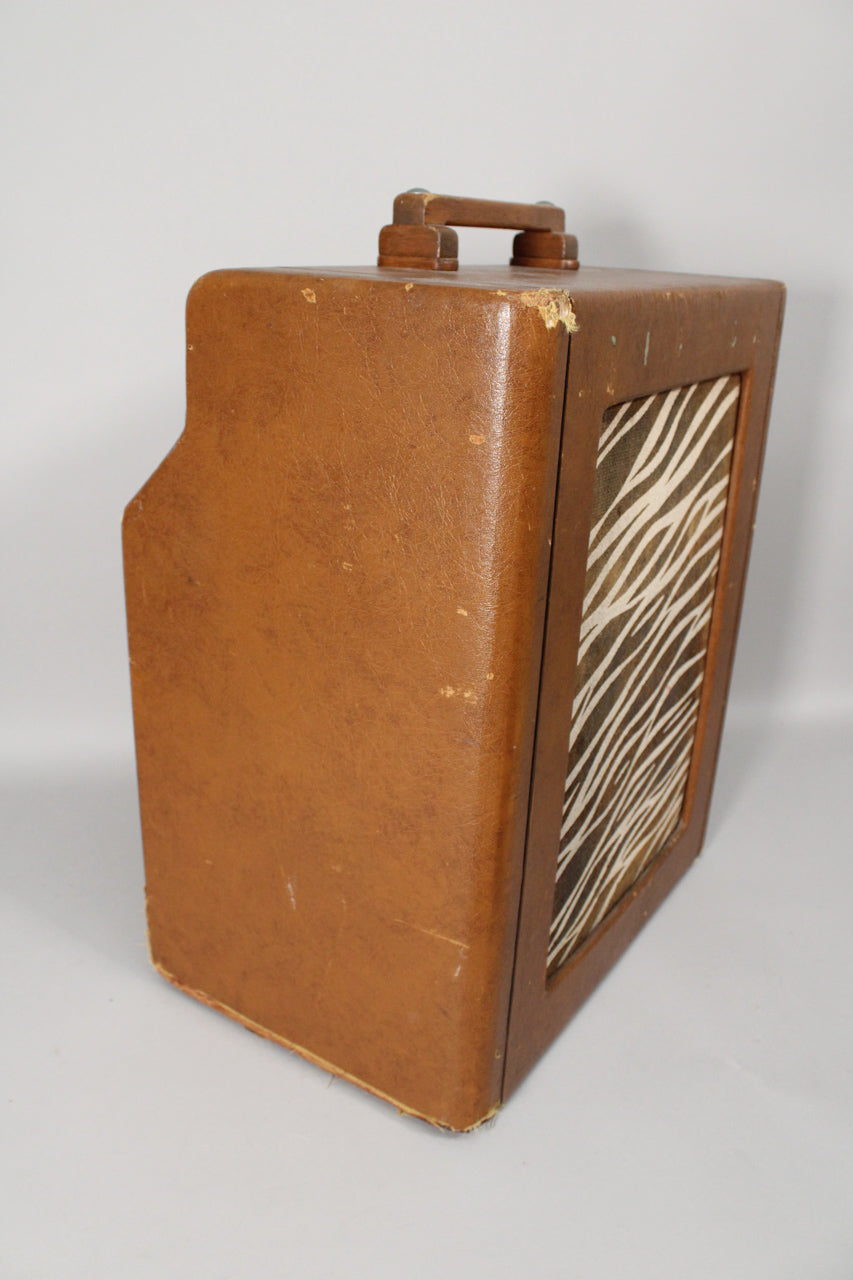 The brown leatherette amp is angled to show its left side, top handle, and a zebra-print speaker grille with some wear.