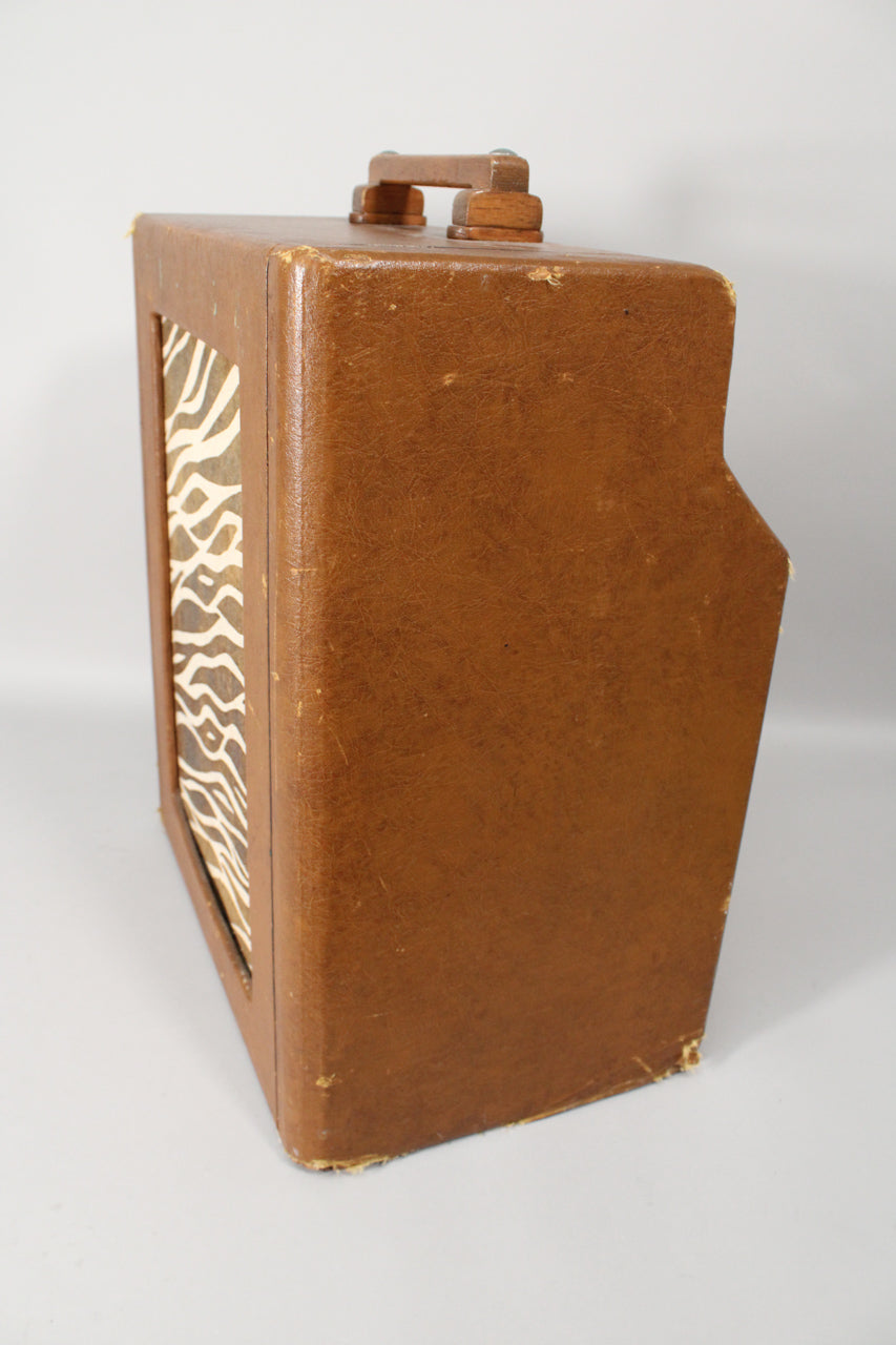 Right-side view of a brown leatherette amp with a wooden handle, showing a zebra-print grille cloth and wear on the corners.