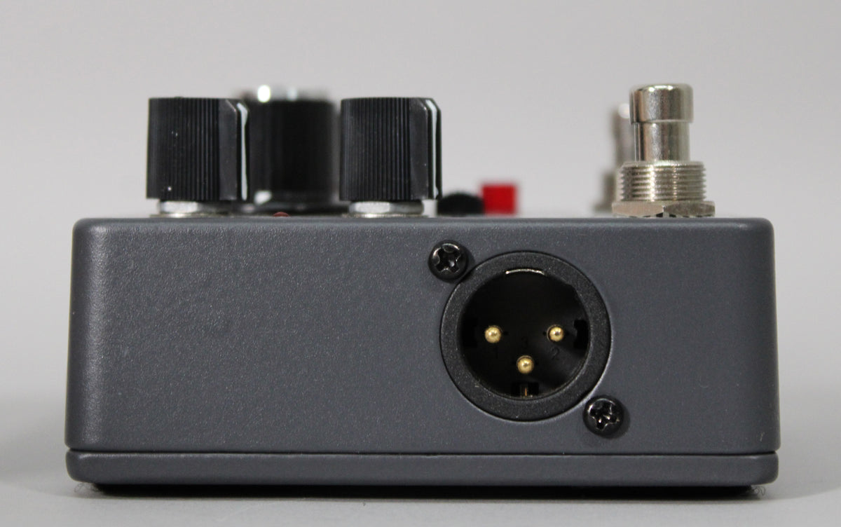 The dark gray pedal is viewed from the right side, showing a 3-pin XLR jack and two black control knobs on top.