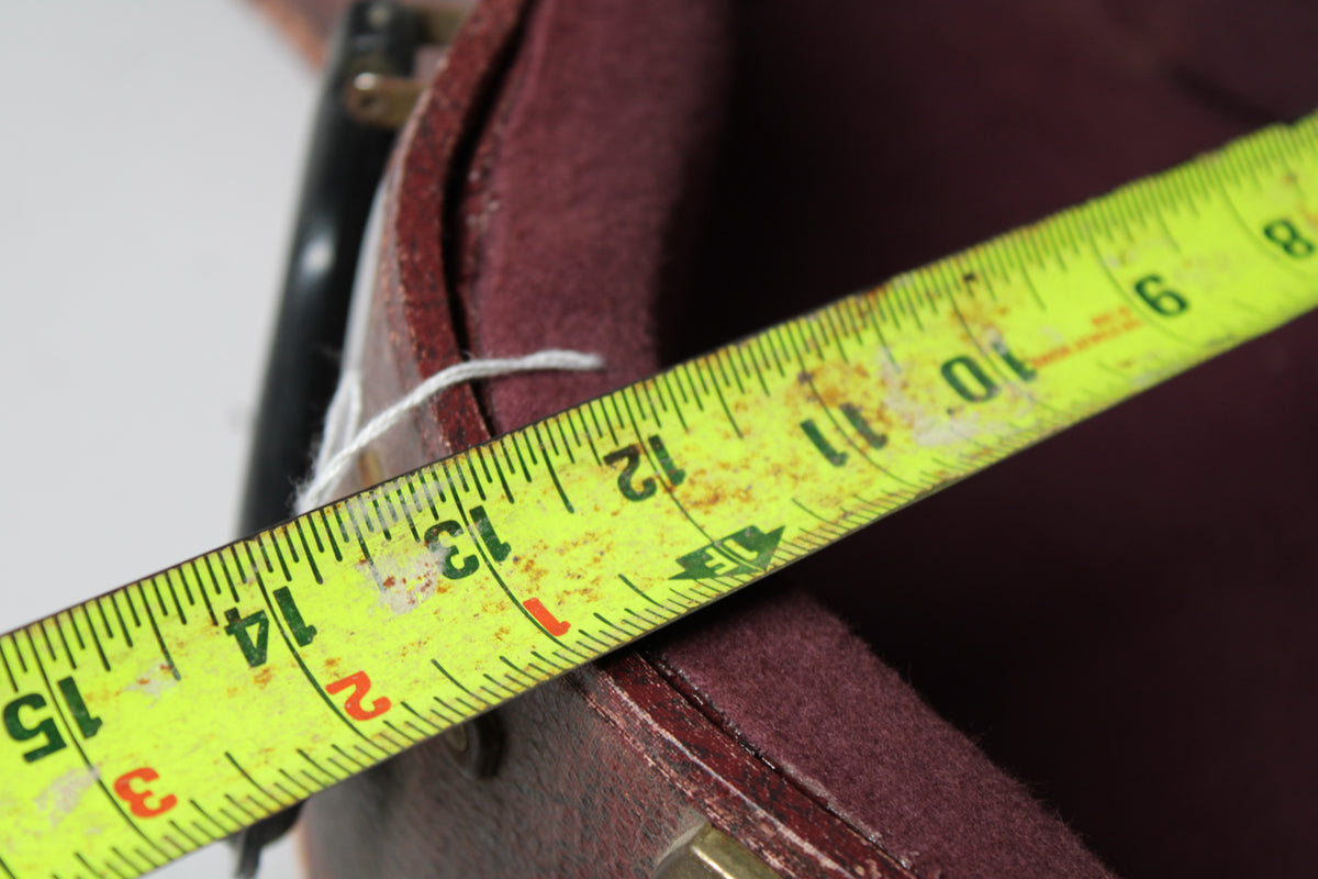 A yellow measuring tape extends diagonally across the open brown snakeskin case, showing the burgundy plush interior.