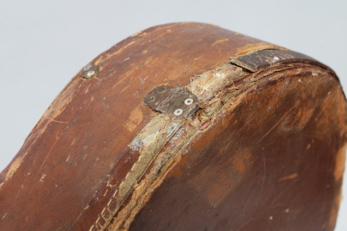 Close-up of the brown case's worn, curved edge, showing exposed wood, peeling material, and a metal hinge plate with two screws.