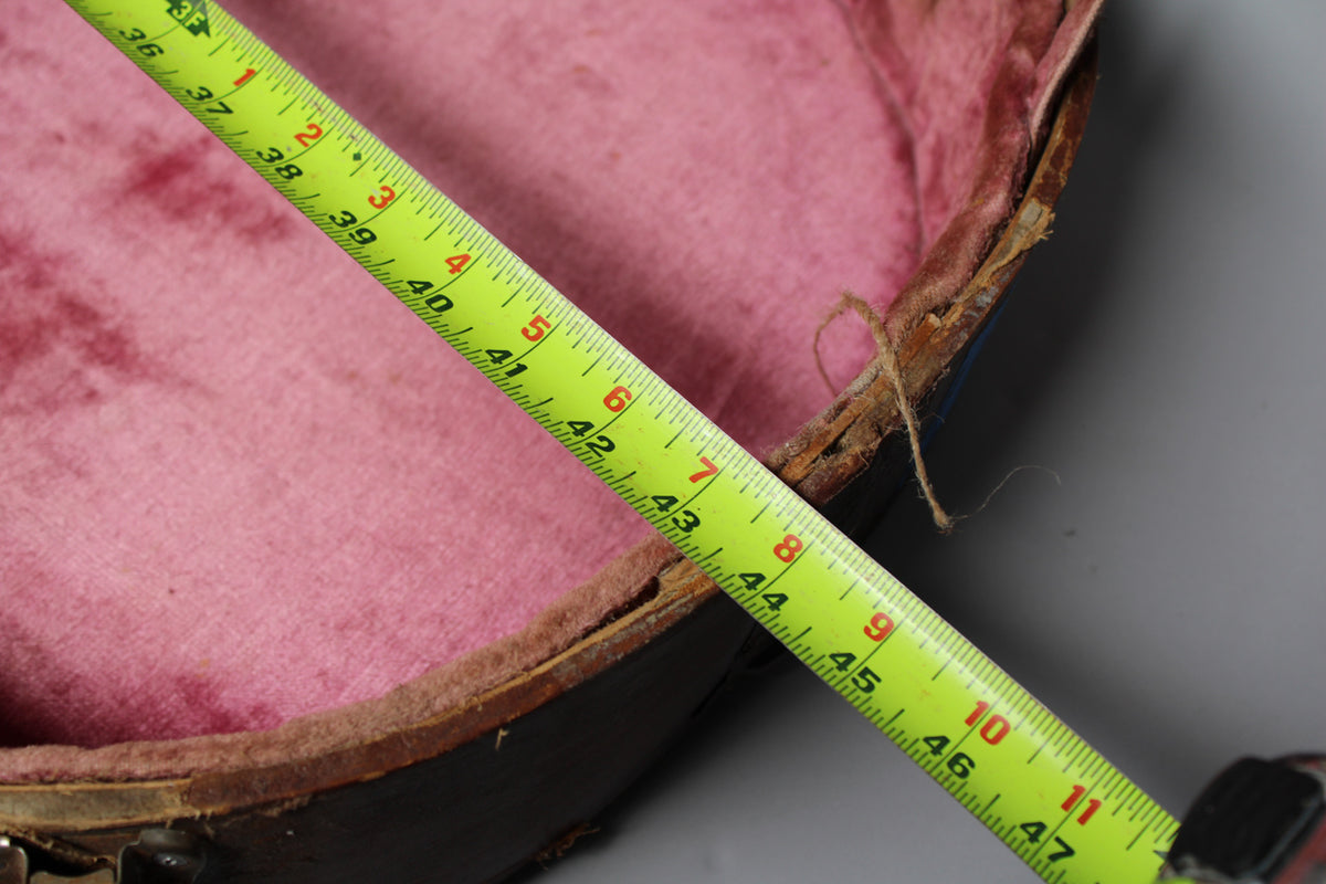 A yellow tape measure stretches across the open brown case, revealing worn pink plush lining and frayed edges.