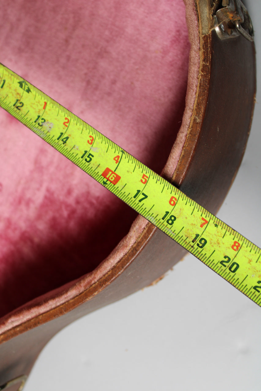 A yellow measuring tape stretches across the open brown case, showing the pink interior and worn edges.