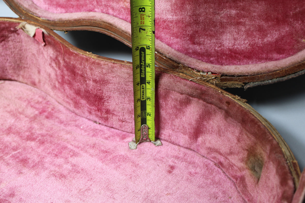 A close-up of the open brown case with worn pink plush lining, showing a measuring tape indicating a depth of 8 inches.