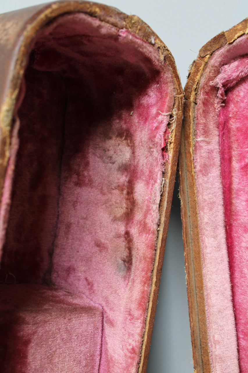 Close-up of the case's open interior, revealing faded pink plush lining with dark wear spots and exposed brown wood edges.
