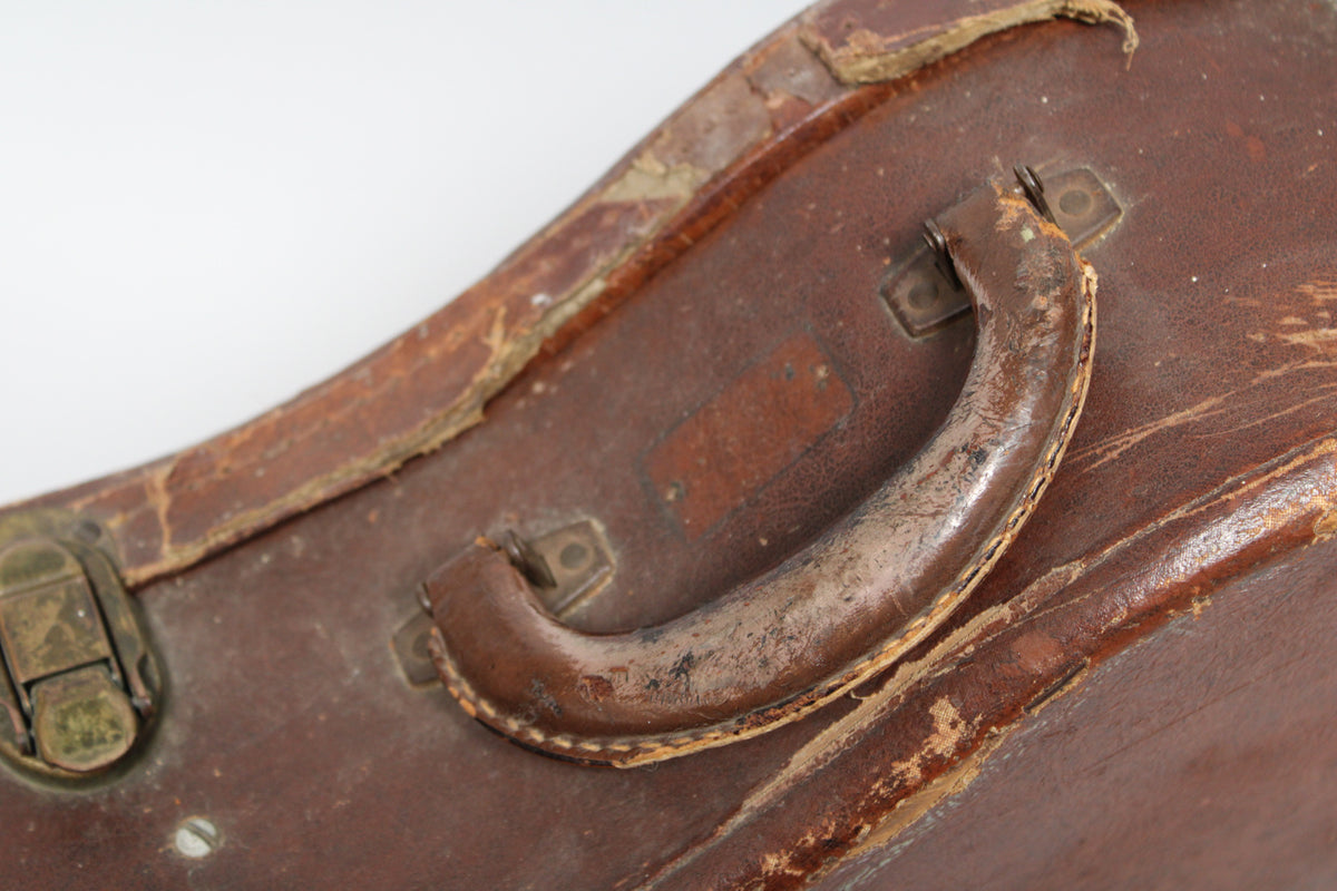 Close-up of the worn brown leather handle and surrounding case, showing heavy scuffing, peeling, and a tarnished brass latch.
