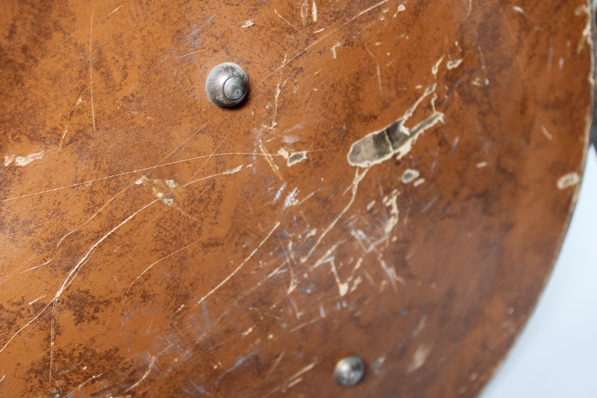 Close-up of the brown case exterior, showing heavy wear, scratches, and a large tear exposing the material underneath, with two metal studs.
