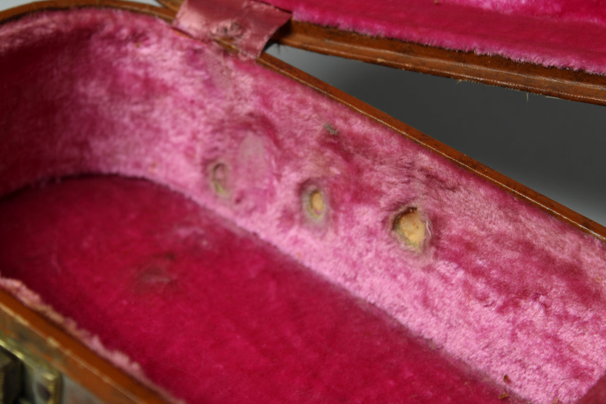Close-up of the case's worn, faded pink plush interior, showing three circular indentations and a small tear near the hinge.