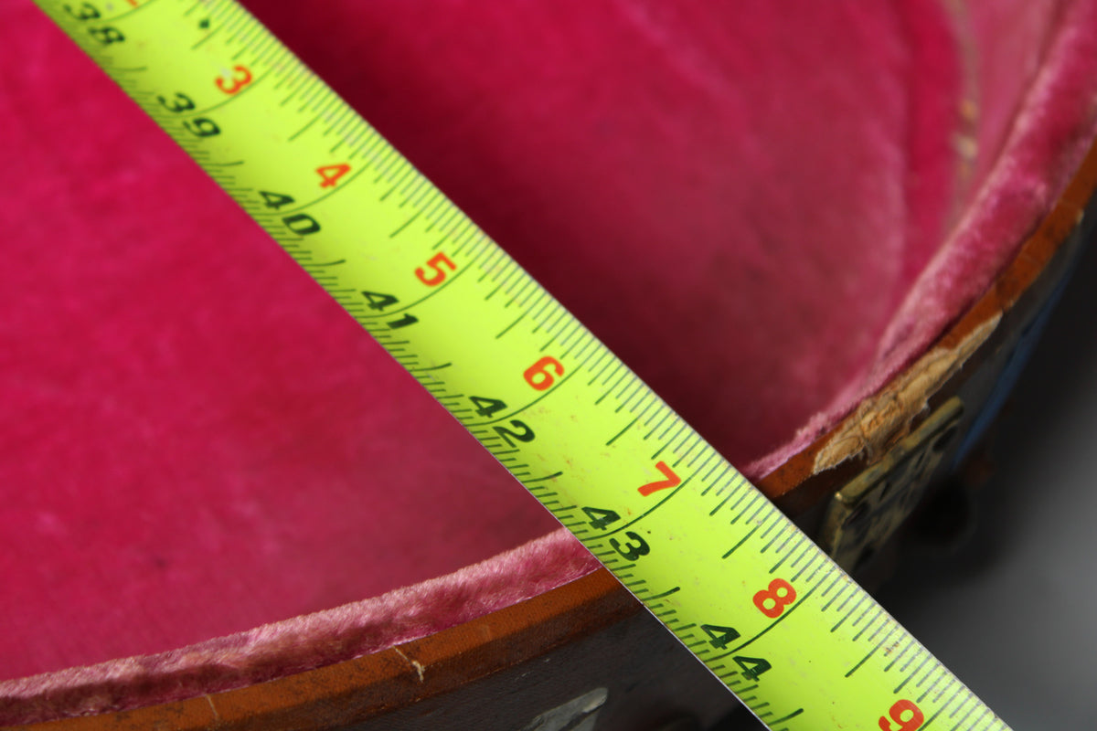 A yellow tape measure spans the open, pink-lined brown case, revealing chipped wood and worn edges near a brass latch.