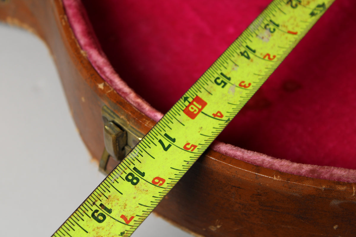 A yellow tape measure spans the open brown case, revealing its deep pink plush interior and a brass latch.