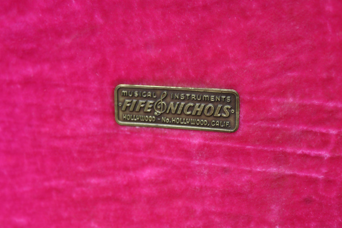 Close-up of the case's vibrant pink plush interior, featuring a brass "Fife & Nichols Musical Instruments" plaque.