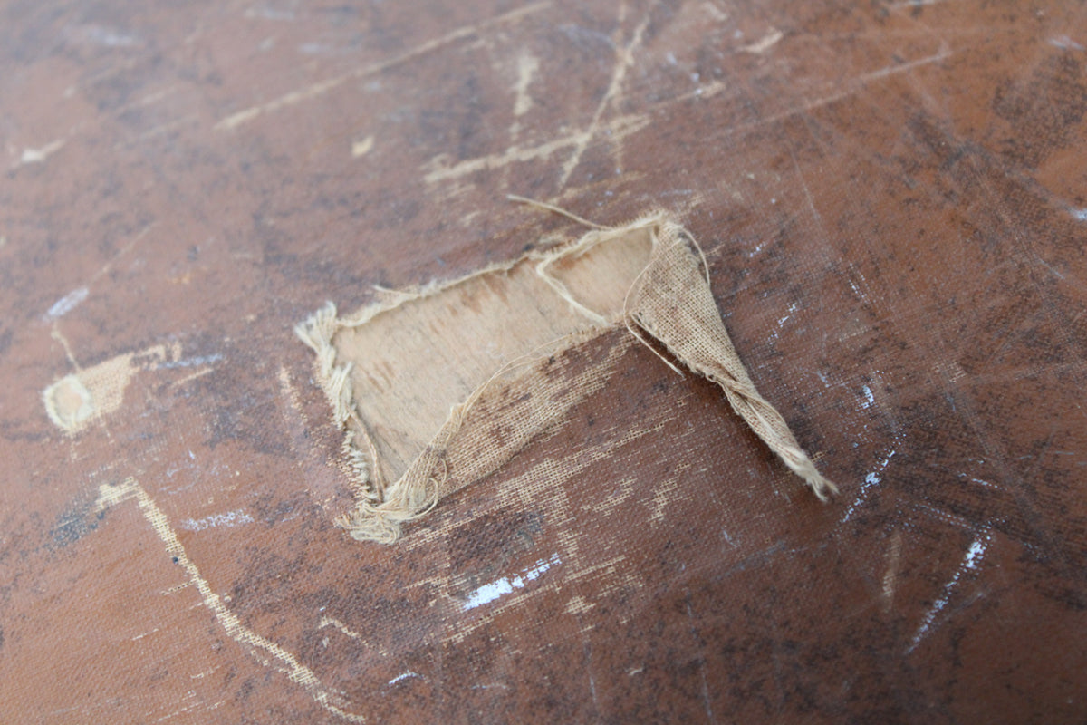 Close-up of the brown case exterior, showing a large tear in the covering revealing the light brown canvas and wood underneath.