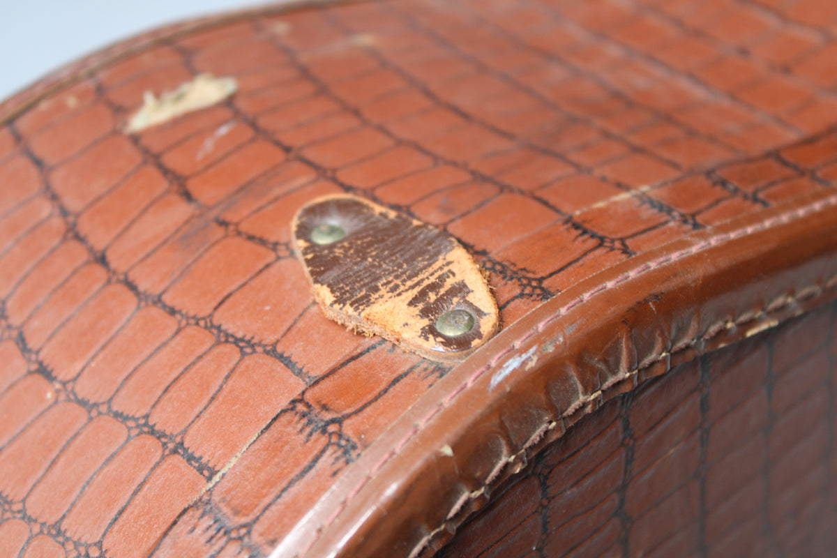 Close-up of the brown alligator-patterned case top, showing a worn leather strap tab with two brass rivets and some surface damage.