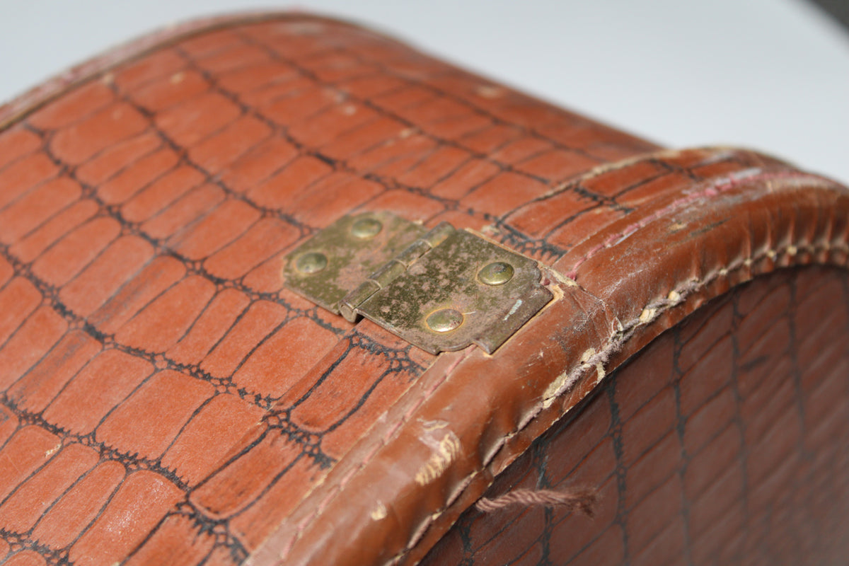 Close-up of the brown alligator-patterned case, showing a tarnished brass hinge and heavy wear along the stitched edge.