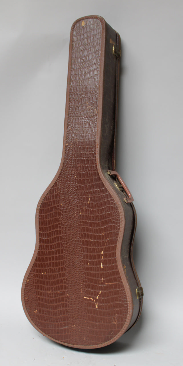 Brown alligator-patterned guitar case, seen from the side, showing a handle, two latches, and scuffs on the textured surface.