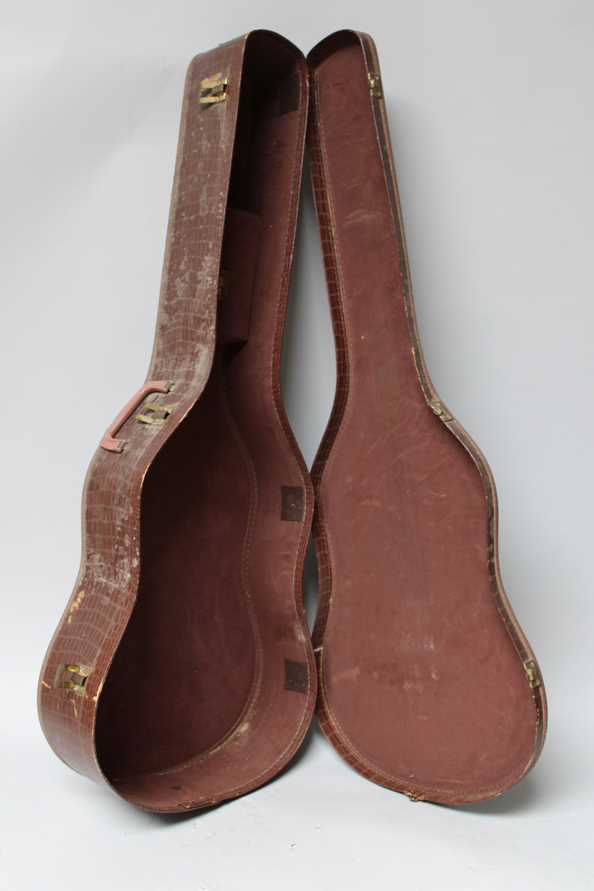Brown alligator-patterned guitar case, open and standing upright, showing its worn, reddish-brown plush interior and brass hardware.