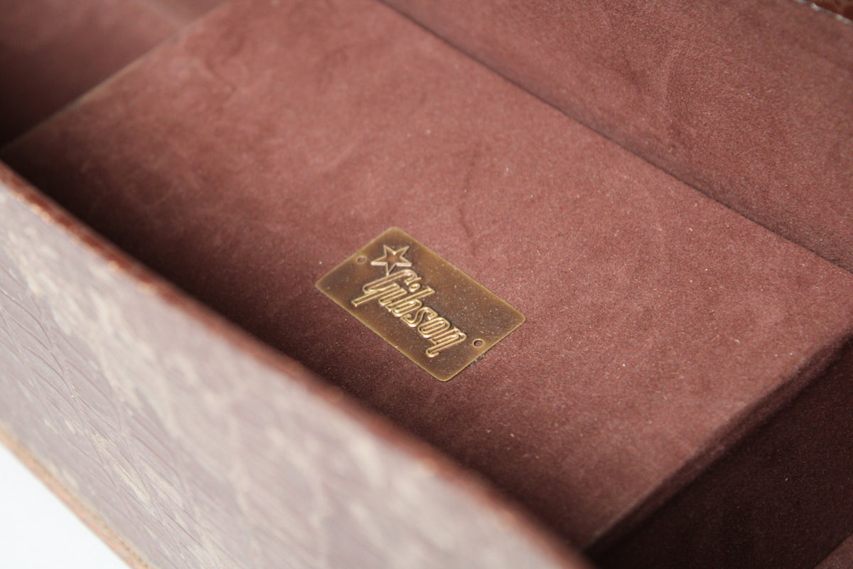 Close-up of the case's interior, showing the worn brown plush lining and a brass "Gibson" logo plate with a star.