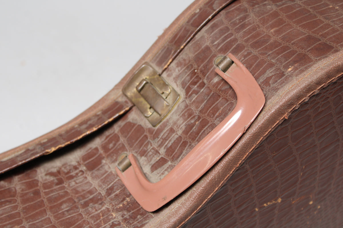 Close-up of the brown alligator-patterned case, showing a pink plastic handle and a brass latch, all with visible wear.