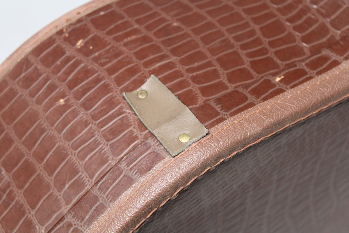 Close-up of the brown alligator-patterned case, showing a light brown leather tab with two brass rivets and some wear.
