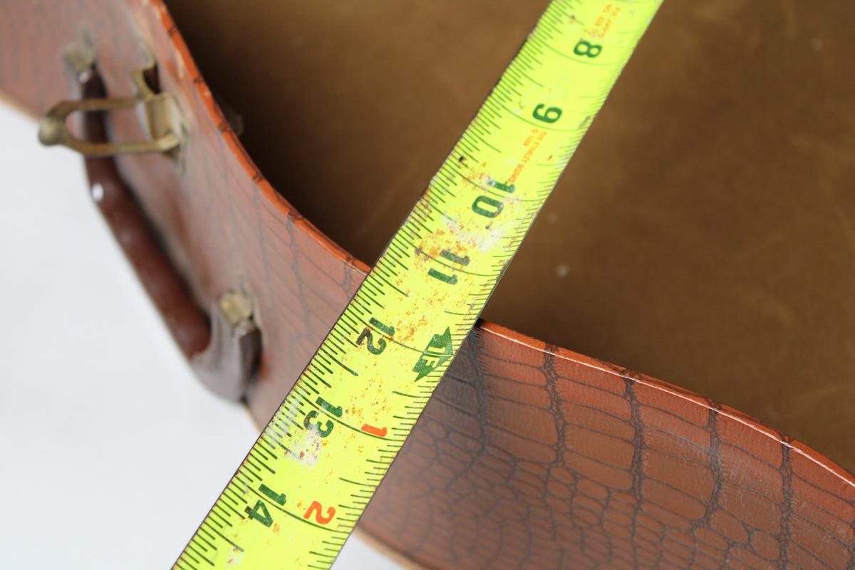 A yellow tape measure spans the open brown snakeskin case, showing its depth and a brass latch on the left.
