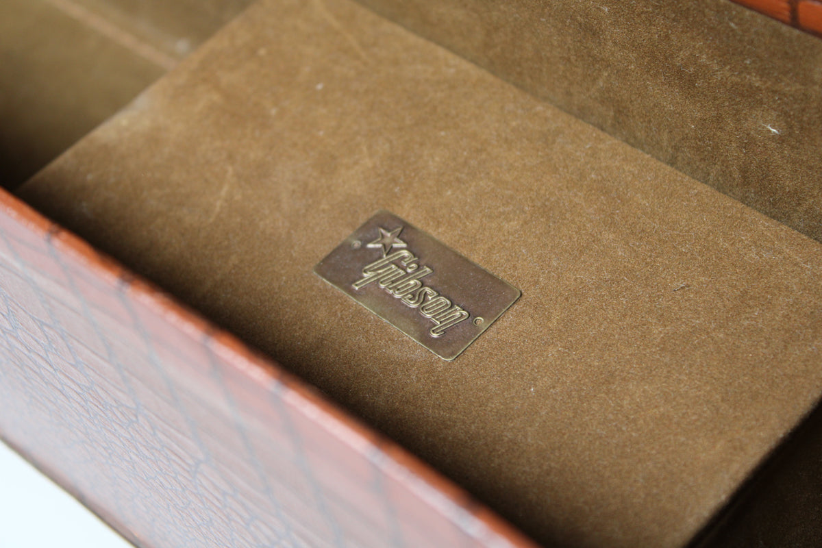 Close-up of the case's open interior, revealing a worn brass plaque on the tan plush lining, with some dust and fibers visible.