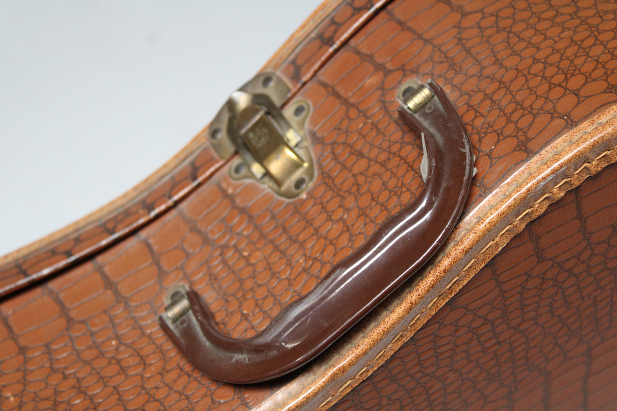 Close-up of the brown snakeskin-patterned case handle and brass latch, showing wear and scuffs on the handle.