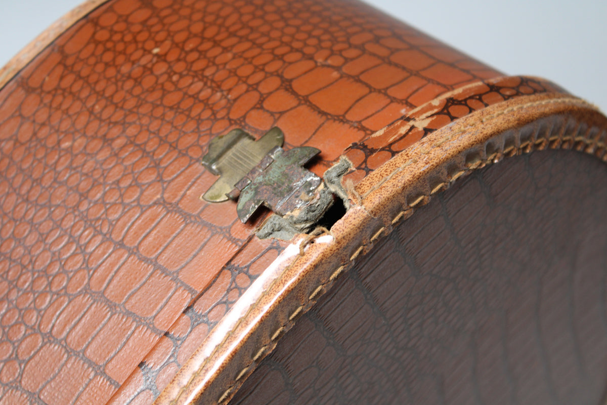 Close-up of the brown snakeskin case, showing a corroded brass latch and a tear in the binding near the case's edge.