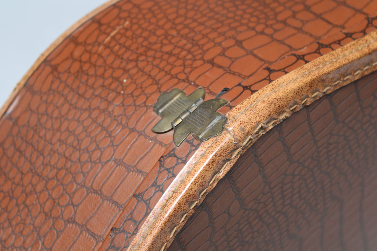 Close-up of the brown snakeskin-textured case with a brass butterfly hinge and visible wear along the stitched edge.