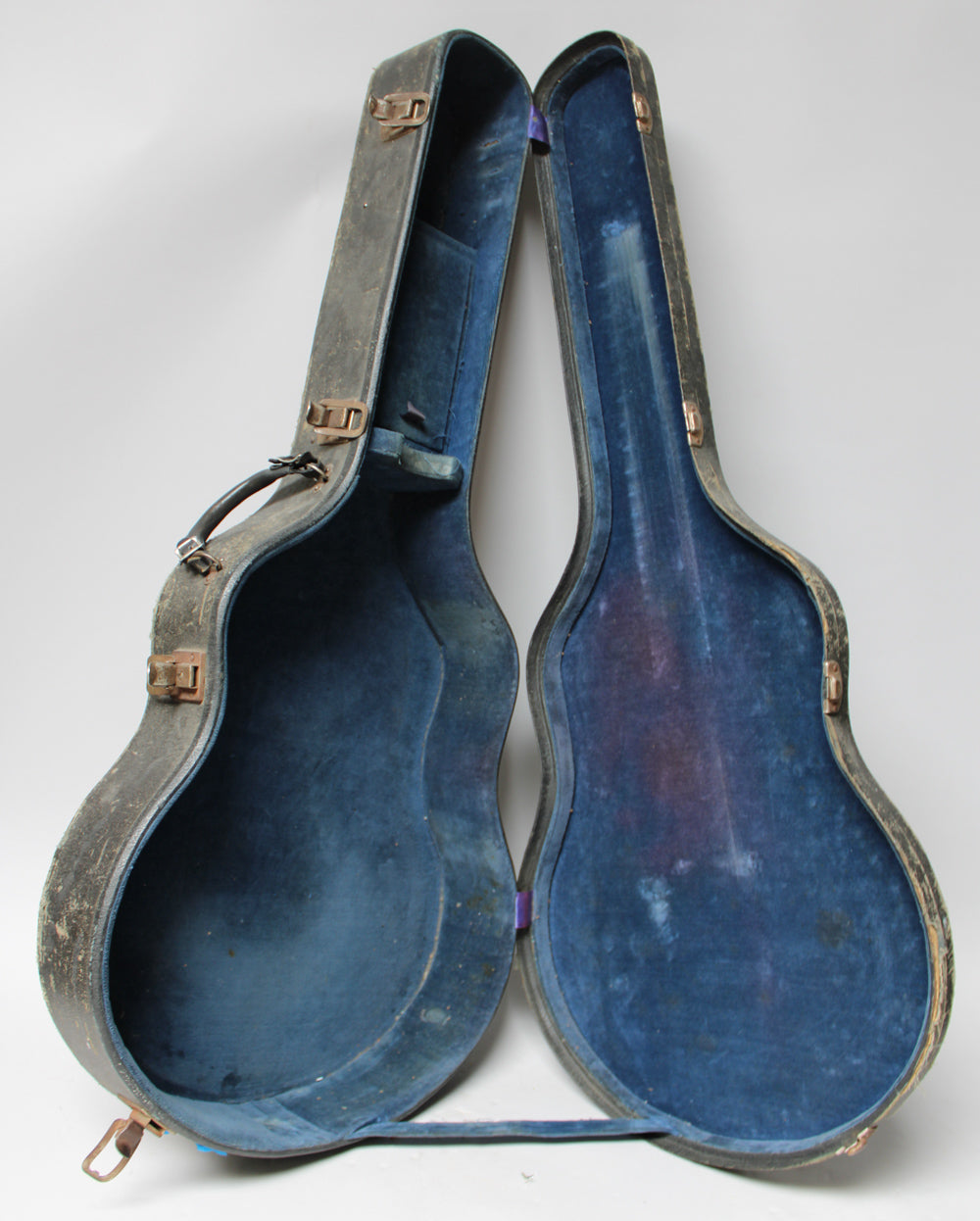 The open black archtop case, lined with faded blue velvet, stands upright, revealing its worn interior and rusty latches.