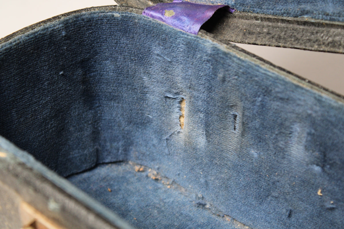 Close-up of the case's worn blue velvet interior, showing a large tear exposing the wood, and a purple ribbon on the lid.