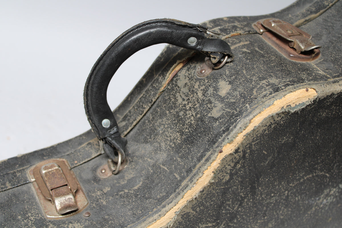 Close-up of the worn black case, showing the leather handle, a rusty latch, and exposed wood along a curved edge.
