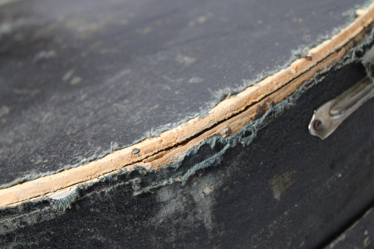 Close-up of the case's worn black exterior, revealing a split seam with exposed wood and frayed blue lining, plus a metal latch.