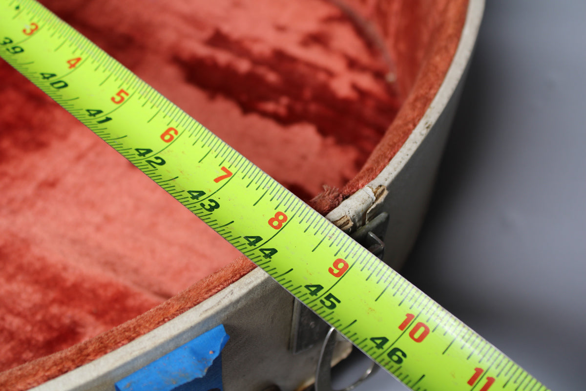 A yellow tape measure spans the open tan case, showing the red velvet interior and worn edges near a metal latch.