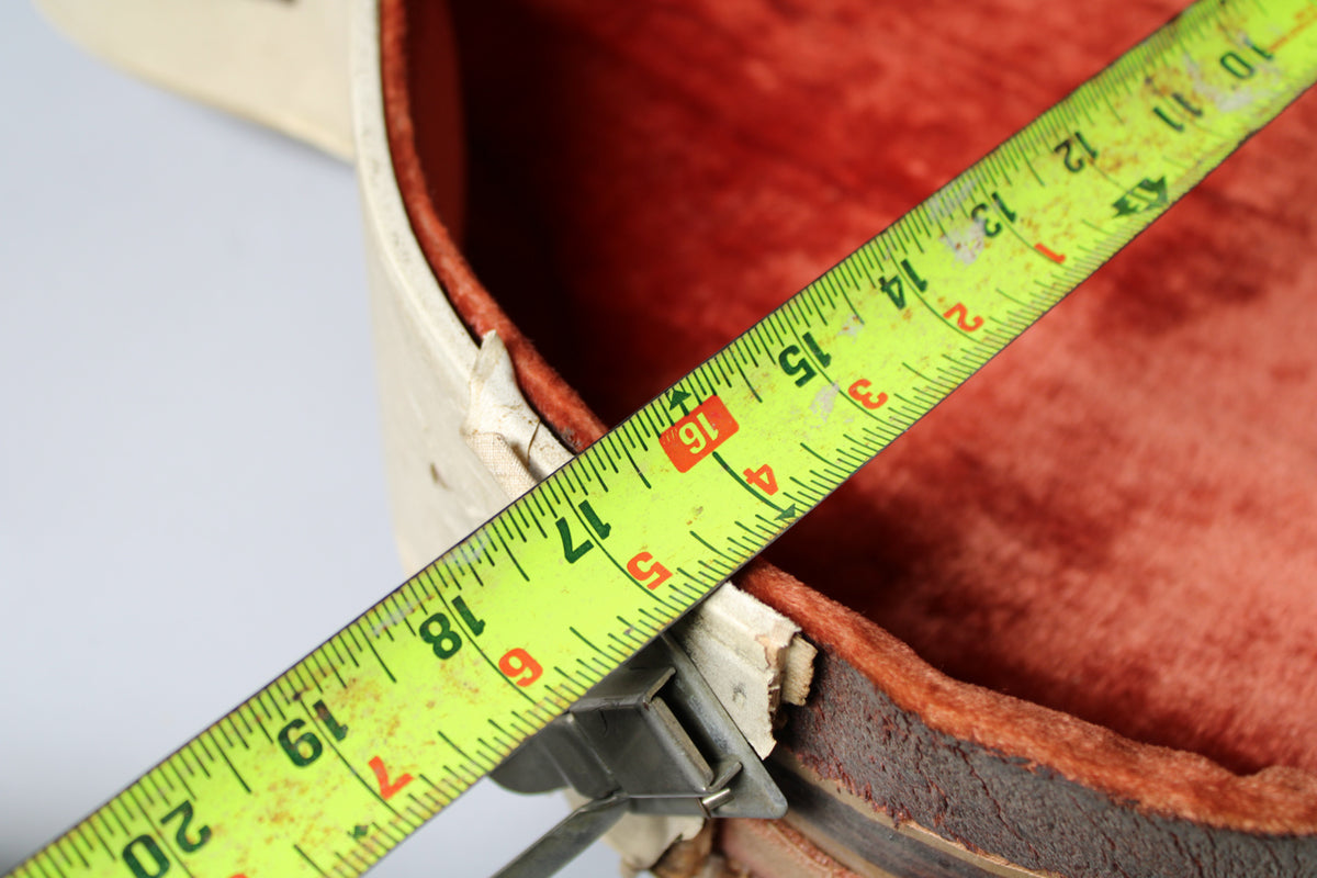 A bright yellow tape measure extends across the open, tan case, showing the red plush interior and worn edges.