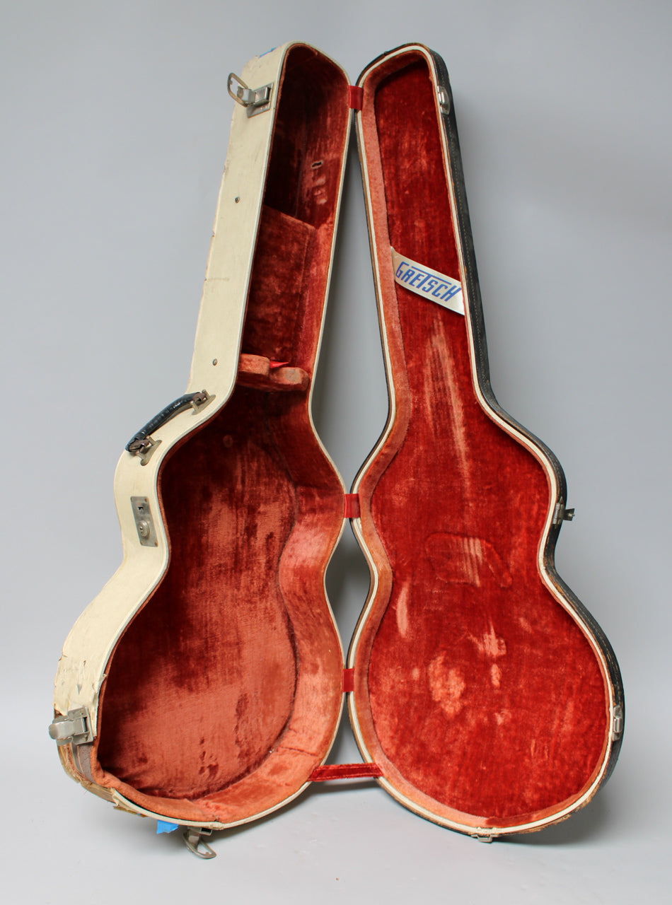 Open tan archtop case with worn red velvet interior, showing a blue Gretsch label and tarnished metal hardware.